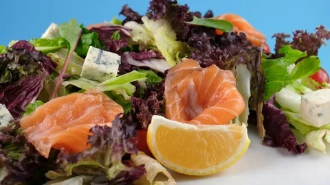 Leaf vegetable salad with smoked salmon, cheese and tomatoes on blue background Stock Footage 78668069