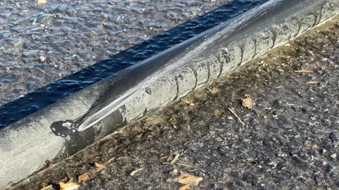 Leaking black polyethylene water pipe on ground outdoors Stock-Footage 276890595
