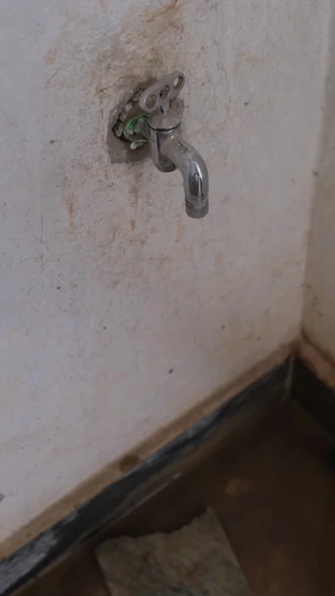 Leaking chrome water tap with dripping water drops on a rough concrete wall 스톡 동영상 332998039