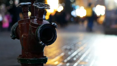 Leaking fire hydrant with walking crowd on background. Old red fire hydrant in Vidéo 122765574