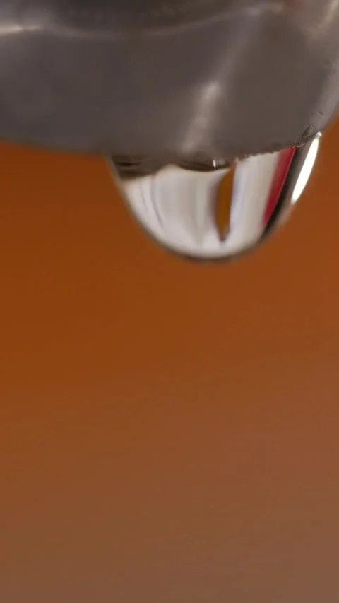 Leaking kitchen faucet dripping water against blurred orange, vertical Stock Footage 341525145