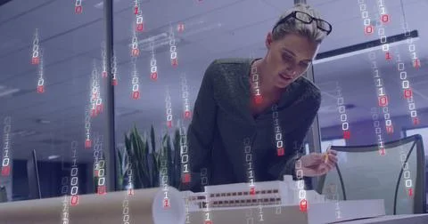 Leaning architect inspecting scale model at office desk with blueprints, binary 写真素材