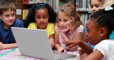Leaning group of six students pointing at silver laptop on patterned table in Stock Photos
