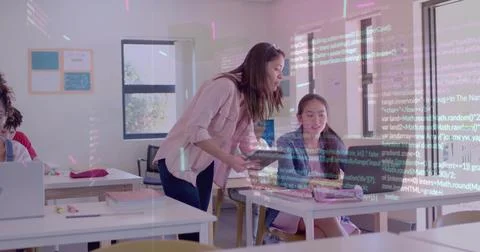 Leaning instructor in pink top pointing tablet at student laptop in school class 写真素材