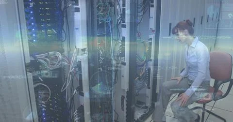 Leaning IT pro inspecting server racks and cables at data center, wearing blue Stock Photos