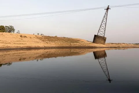 Leaning Power Pole Reflected in River at Sunset over a Sandy Bank Stock Photos