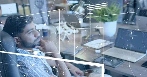 Leaning South Asian man processing network data at modern office desk, with Foto stock