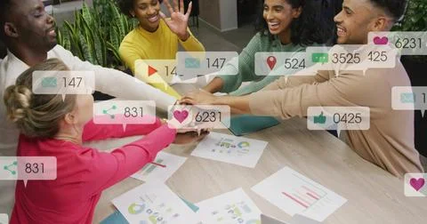 Leaning team of five stacking hands at office table, in bright tops, with Stock Photos
