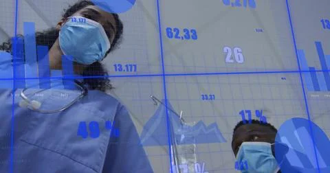 Leaning two masked staff checking camera in clinic, with blue scrubs, masks, IV Stock Photos
