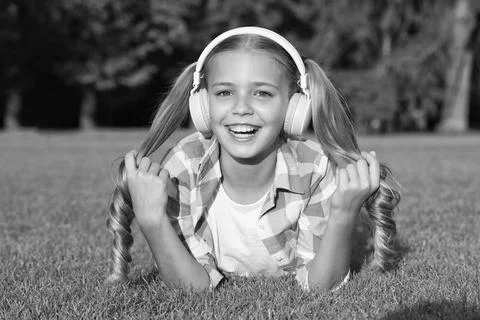 Learn any language in fun way. Happy kid wear headphones lying on green grass Foto stock