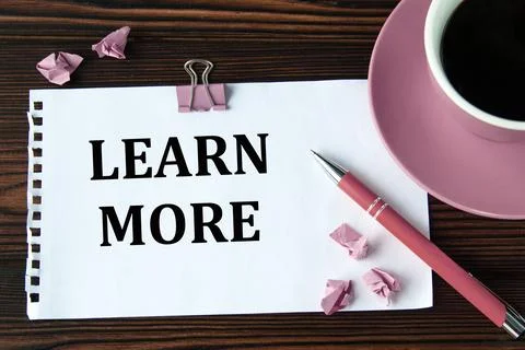 LEARN MORE - words on a white sheet on a wooden brown background with a cup.. Stock Photos