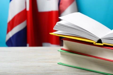 Learning foreign language. Different books on wooden table near flag of Uni.. Stock Photos