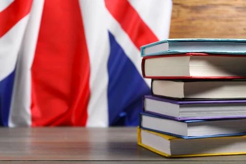 Learning foreign language. Different books on wooden table near flag of Uni.. Stock Photos