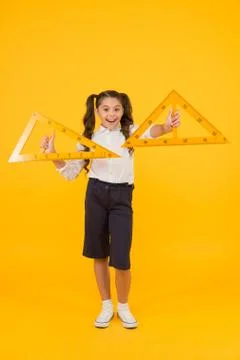Learning geometry in school. School kid holding measuring instruments on yellow Stock Photos