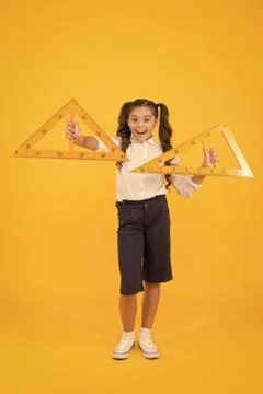 Learning geometry in school. School kid holding measuring instruments on yellow Stock Photos