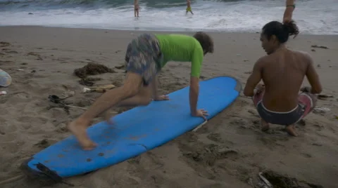 Learning how to get up on a surf board during a beginning surf lesson Stock Footage 58930545