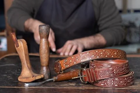 Leather belts with leather tools on table and craftsman working behind Stock Photos