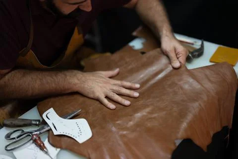 Leather crafting in progress: artisan hand smoothing brown leather on work table Stock Photos