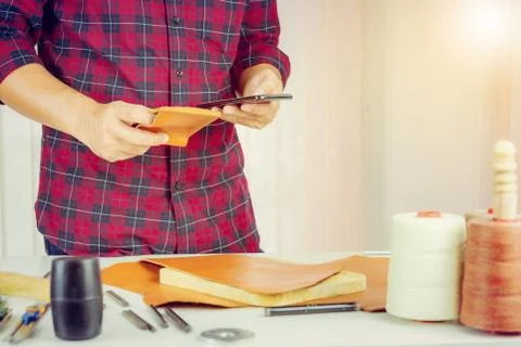 Leather craftsman using mobile smartphone and holding wallet Photos