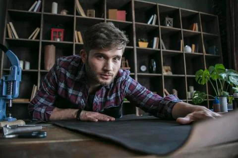 Leather maker sitting at working table with black leather. Young man Stock Photos