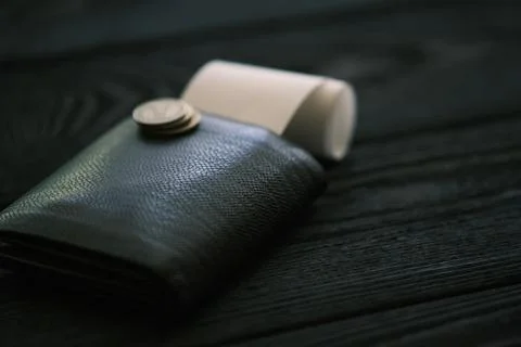 A leather purse and small stack of coins on black wooden table Foto stock