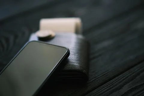 A leather purse and small stack of coins on black wooden table Stock Photos