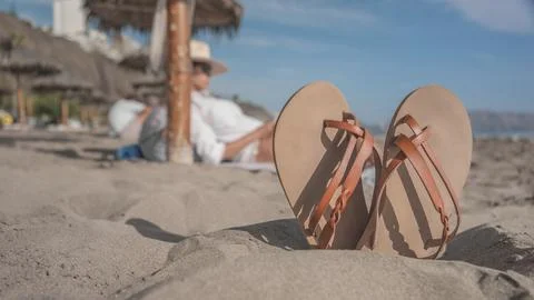 Leather sandals standing on the beach while relaxes reading a book Stock Photos