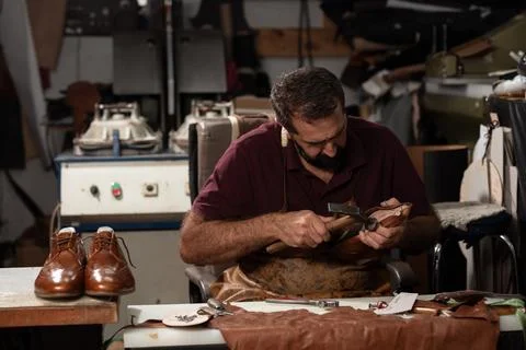Leather shoemaker at work in a busy workshop shaping leather, with brown leather Stock Photos