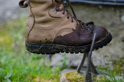 A leather walking boot, being cleaned on an old cast iron boot scraper. 库存照片