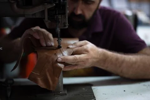 Leather work in progress: skilled craftsman sewing brown leather piece with Stock Photos