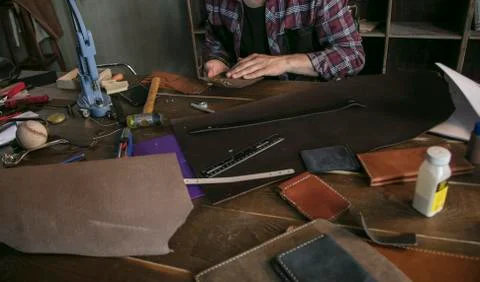 Leather worker man sitting behind table with tools and holds leather key case Stock Photos