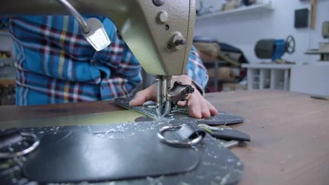 A leathersmith stitches or sews a black leather clutch bag on a sewing machine Stock Footage 152185480