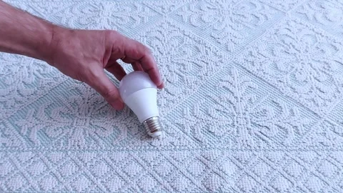 LED Bulb Gripped Over Patterned Fabric: Close-Up Lighting Study Vídeos de archivo 311695335