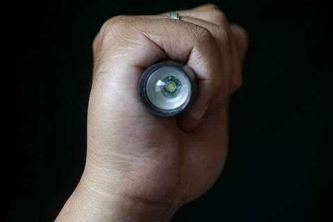 An LED flashlight held in a person's hand on a black background. Close up vie Stock Photos