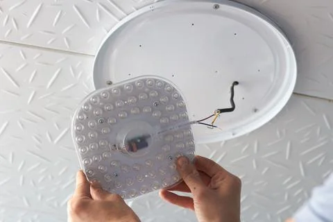 LED lamp on the ceiling a man's hand holds in the middle on a light backgroun Stock Photos