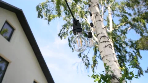 LED light bulb hanging on a wire near the white country house and a tree Stock Footage 278484399