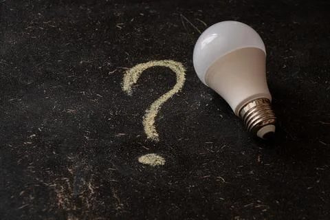 An LED light bulb next to a drawn question mark on a dark background, on th.. Stock Photos