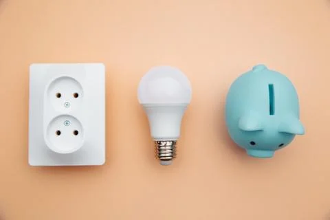 LED light bulb, power socket and blue piggy bank. Power energy economy concept Stock Photos