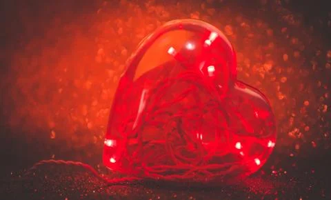 Led lights inside plastic heart with defocused red glitter background. TONED  Stock Photos