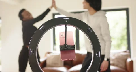 LED ring light framing diverse friends high-fiving behind phone mount in living Stock Footage 340986900