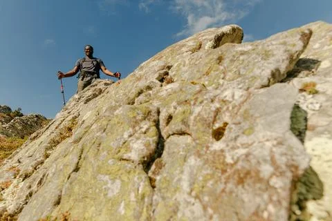 Left-of-center wide angle from below looking up at black hiker with his walking Stock Photos