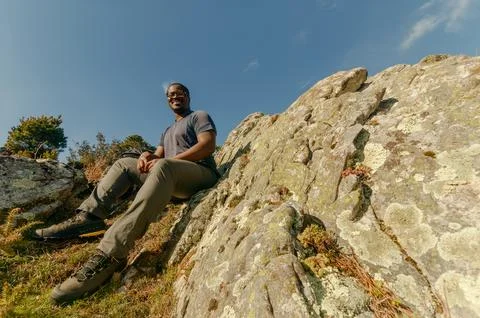 Left-of-center wide angle from below looking up at smiling black hiker sitting Stock Photos