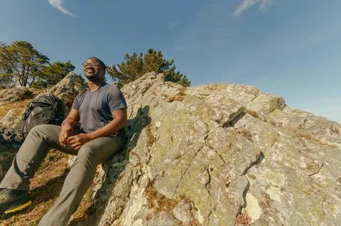 Left-of-center wide angle from below looking up at smiling black hiker sitting Stock Photos
