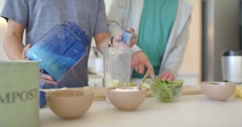 Left cook scooping powder into blender cup while right person cutting fruit for Video stock 344656127