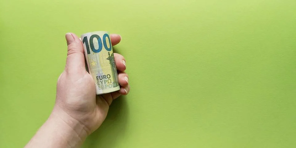 Left hand holding rolled up bundle of 100 Euro banknotes on green background Stock Photos