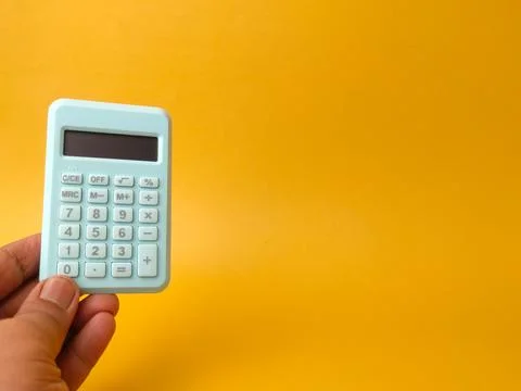 A left hand holds a small, light blue electronic pocket calculator on the s.. Stock Photos