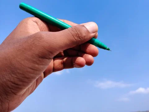 Left hand Man using green ink pen to write. Cloud background. Stock Photos