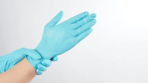 Left hand is pulling blue latex gloves on white background. Stock Photos