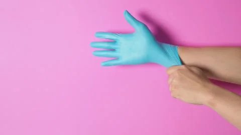 Left hand is pulling blue latex glove of the right hand on pink background. Stock Photos