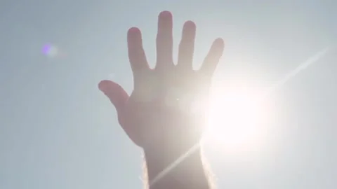 Left hand reaching up towards the sun in blue sky Stock Footage 346026906